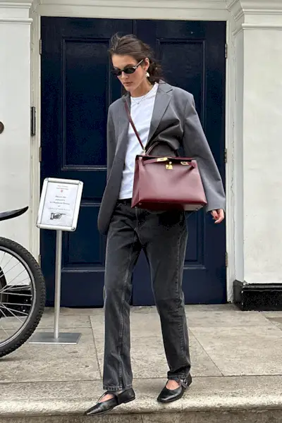 a photo showing what shoes to wear with bootcut jeans, specifically a woman wearing a gray blazer over a white t-shirt with black bootcut jeans and black ballet flats