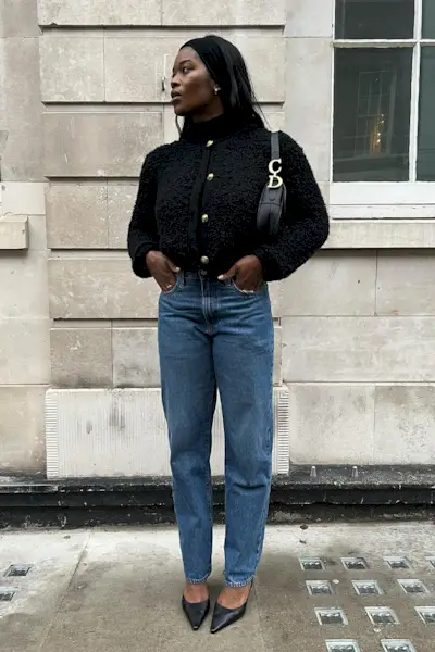 a photo showing what shoes to wear with bootcut jeans, specifically a woman wearing a black tweed jacket with a black dior bag, dark wash bootcut jeans, and pointed black mules