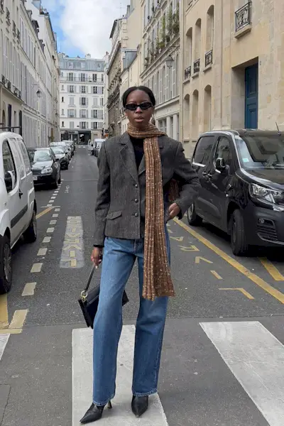a photo showing what shoes to wear with bootcut jeans, specifically a woman wearing blue bootcut jeans with a brown blazer, brown scarf, and brown ankle boots
