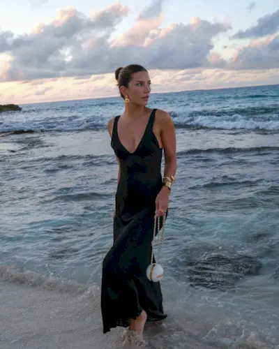 A woman wearing a black V-neck slip dress in the ocean.