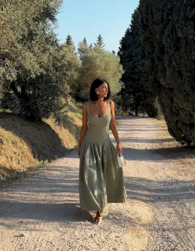 A woman wearing a green drop-waist linen dress with a white mini bag walking on a dirt track.