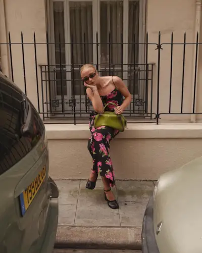 A woman wearing a black-and-pink floral spaghetti-strap maxi dress with a green handbag and black net heels.