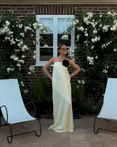 A woman wearing a strapless, maxi-length yellow dress with a large black floral brooch.