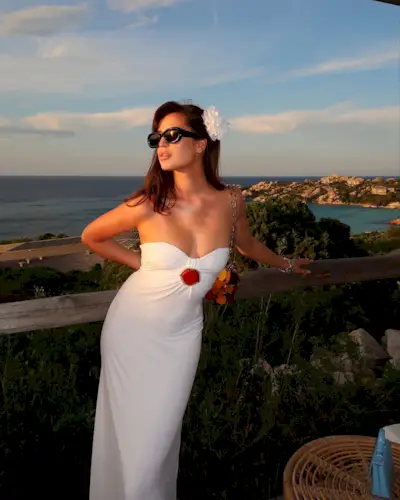 A woman wearing black sunglasses, a white hair clip, and a strapless white maxi dress.