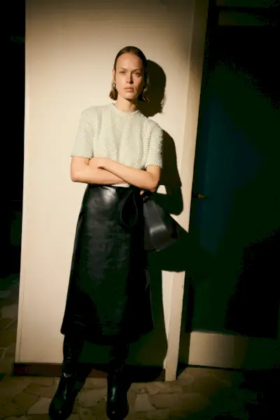 A woman wears a short sleeve shirt, black leather skirt, and black boots.