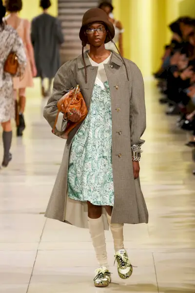 Model walking in the F/W 25 Miu Miu show during Paris Fashion Week wearing a plaid car coat with a floral dress.