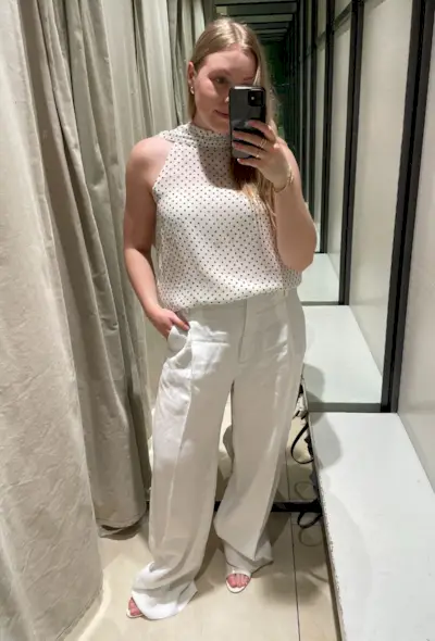 Woman wears polka dot top, white linen trousers and white heels