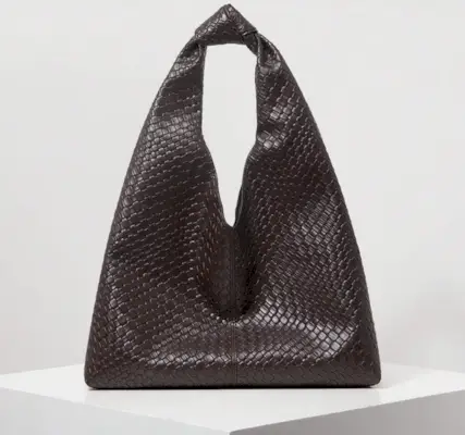 Influencer stands in front of Parisian brick wall wearing white frilly blouse and tailored black pants.