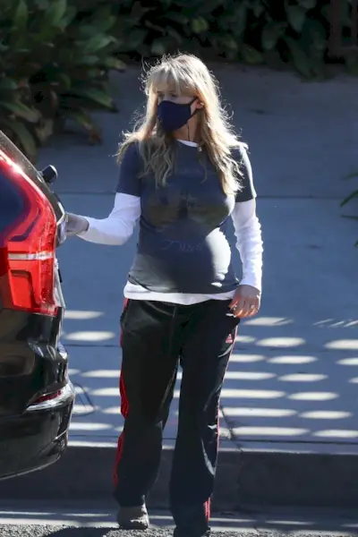 Jennifer lawrence wears a mask, white long-sleeve shirt, graphic t-shirt, and black adidas track pants.