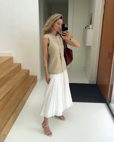@anoukybe wearing a pleated white skirt with a long beige vest