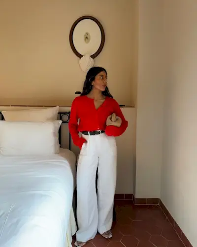 @monikh wearing white trousers and a red cardigan