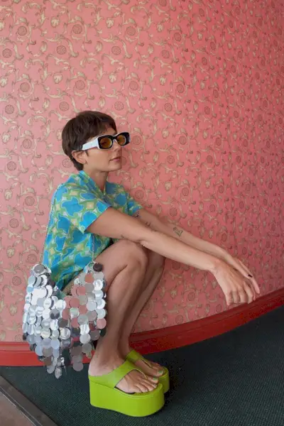 a casual party outfit shown on a woman wearing a vibrant printed button-down shirtdress with green platform thong sandals and a sequin bag