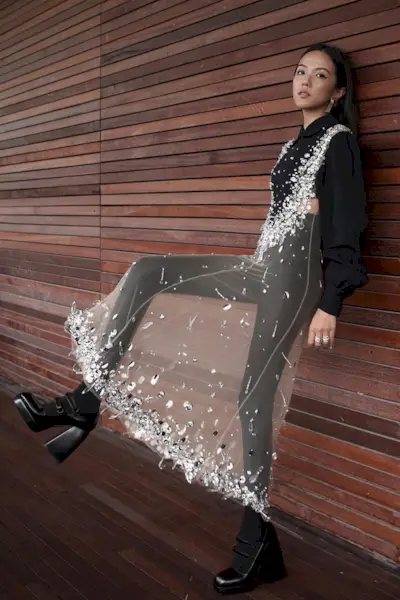 a casual party outfit shown on a woman standing outside wearing a sheer dress over a black cropped button-down shirt with leggings and black platform boots