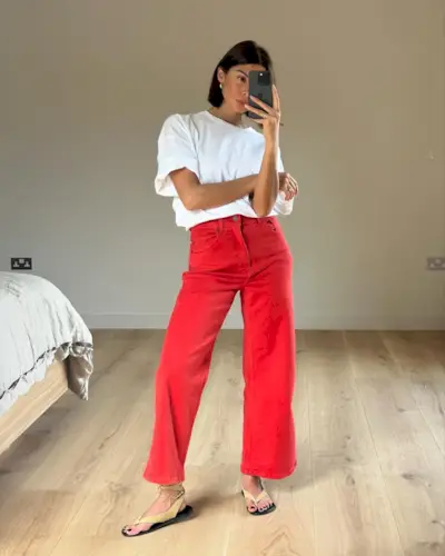British fashion influencer Marianne Smyth poses for a mirror selfie wearing an oversize white T-shirt, red cropped jeans, and tan suede The Row sandals