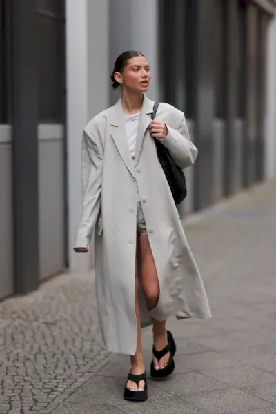 Influencer wears platform flip-flops with an overszied lightweight coat in a light grey shade and tonal micro shorts.