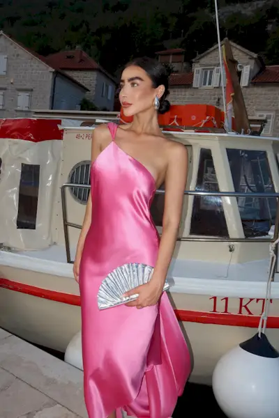 a photo showing cocktail attire for women with a woman wearing a pink gown with a silver clutch bag