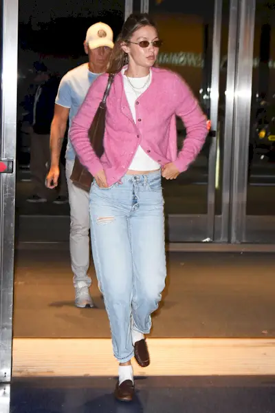 Gigi Hadid wearing a pink cardigan, white T-shirt, jeans, and loafers with socks at JFK.