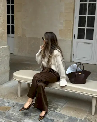 Olivia wears a white sweater, brown silk pants, and leopard slingbacks.