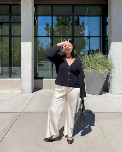 @marina_torres wears a pair of cream satin trousers with a black cardigan and ballet flats