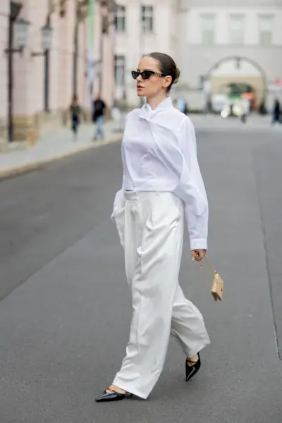 A woman wears a pair of cream satin tailored trousers with a white blouse