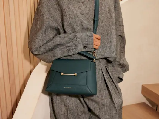 a model wears a gray outfit with a dark green crossbody bag by Strathberry