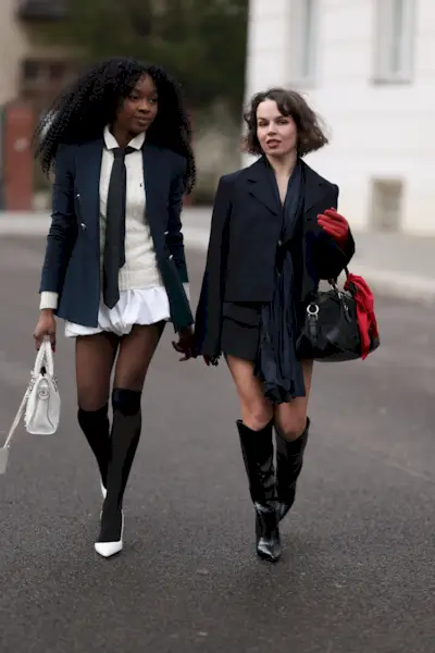 A woman wears a blazer, white blouse, black tie, and bubble shorts.