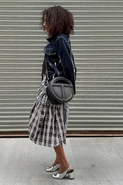 A woman wearing a denim jacket, plaid skirt, and silver shoes