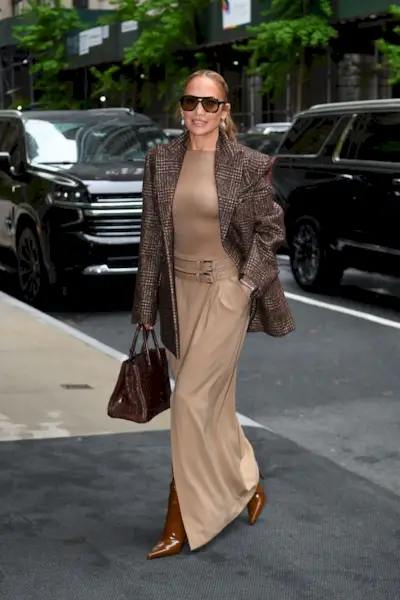 Jennifer Lopez wears a tweed blazer, beige top, beige skirt and patent brown boots and brown saint laurent sac de jour bag