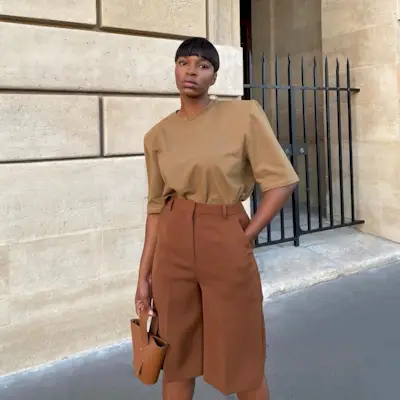 A woman with short hair wearing a brown t-shirt and brown long shorts.