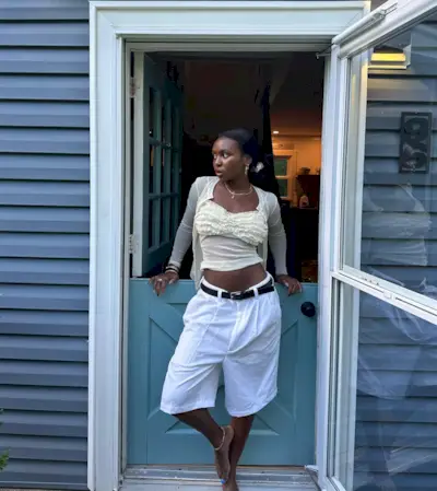 A woman wearing a tank top and cardigan with baggy, long shorts.