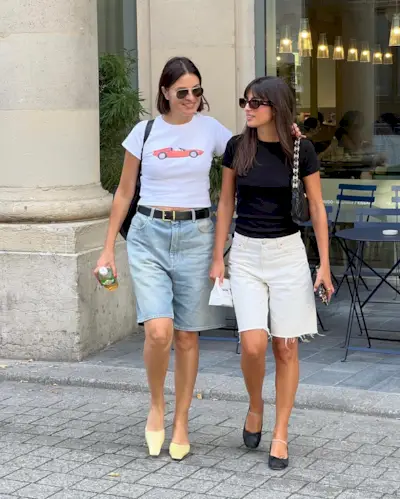 Two women walking toward the camera wearing long denim shorts and t-shirts.