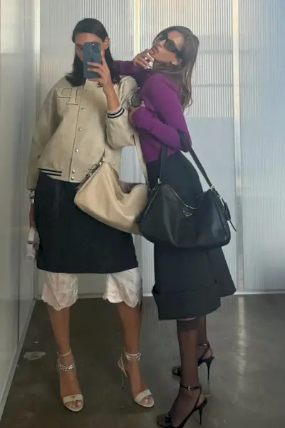 A woman wearing a purple sweater, black skirt, and black leather bag