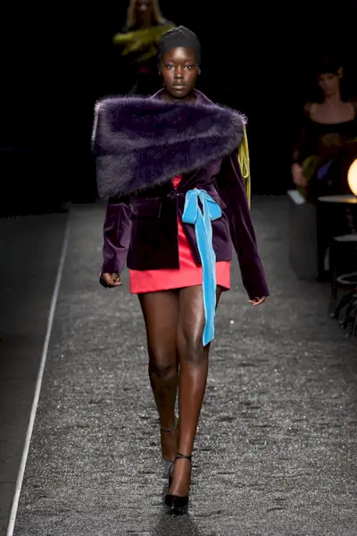 A Nina Ricci model wearing a purple shrug and blazer over a red dress