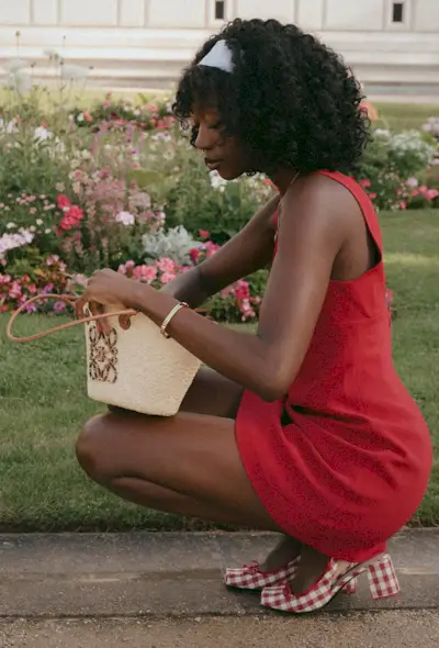 a photo of a woman wearing a red mini dress with plaid slingback heels and a raffia bag