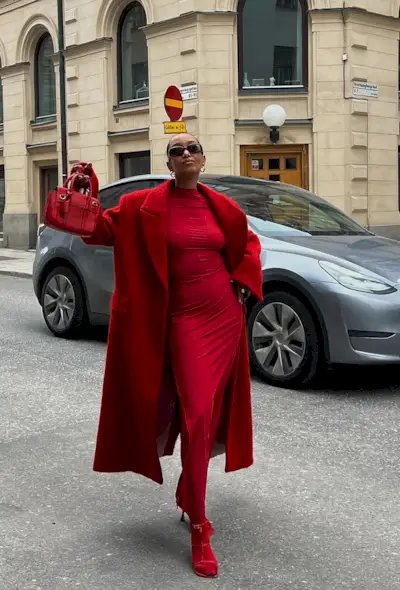a photo of a woman wearing a red coat over a red dress with red tights and red heeled sandals