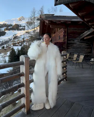 Emma wears a white fur coat, white moon boots, and a white ski suit.