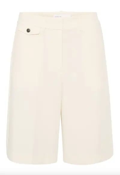 Woman wearing boxer shorts with trench coat and loafers.