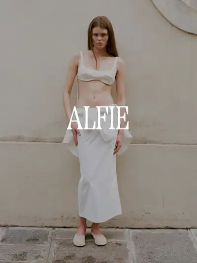 A photo from Alfie's lookbook of a model wearing a bra and white skirt. Text says 'Alfie' in white capital serif letters.