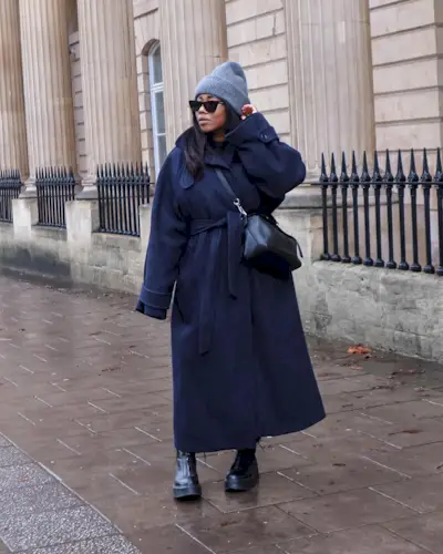 Woman wearing navy coat, black bag, gray beanie, and black zippered chunky Chelsea boots.