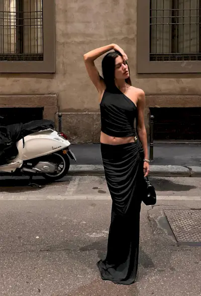 a black maxi skirt outfit showcasing a woman wearing an asymmetrical top styled with a ruched maxi skirt, black handbag, and heels