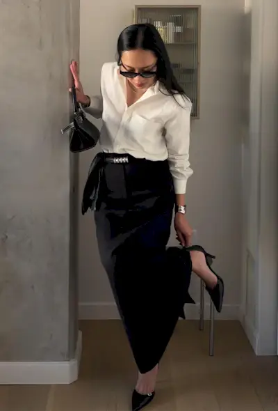 a black maxi skirt outfit shown on a woman wearing a white button-down shirt with a black belt, bag, long fitted black skirt, and black pointed pumps