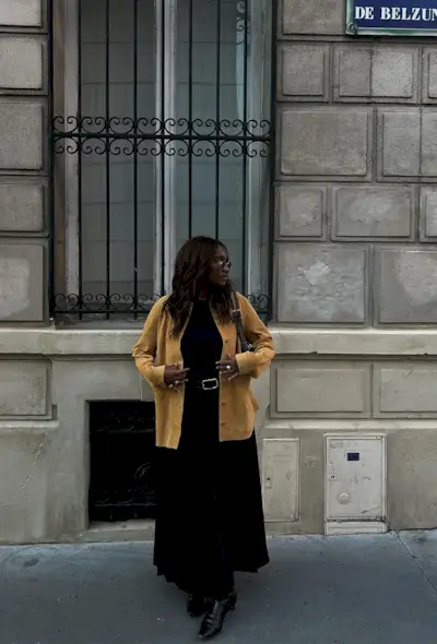 a black maxi skirt outfit showcasing a woman wearing a yellow suede jacket over a black top with a black pleated maxi skirt and black ankle boots