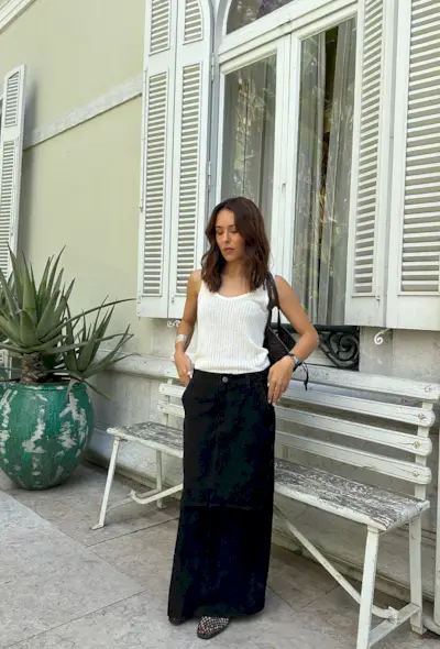 a black maxi skirt outfit showcasing a woman wearing a white knit tank top with a silver bangle, black bag, black maxi skirt, and black fishnet flats
