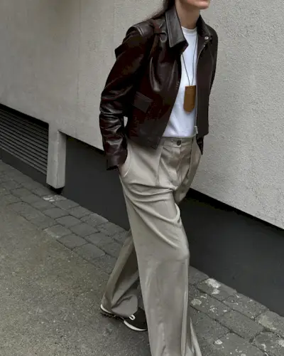 Annabel wears a short leather jacket, white t-shirt, beige trousers, and black sneakers.
