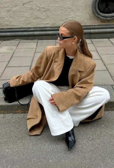 @haaannajohansson wears a tan wool coat, black jumper, white jeans and black ankle boots