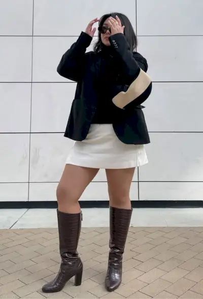 @marina_torres wears a black blazer, white mini skirt, brown knee-high boots and a shoulder bag