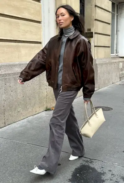 @vikilefevre wears a brown leather bomber, grey roll-neck jumper, grey trousers, white heels and a butter yellow bag