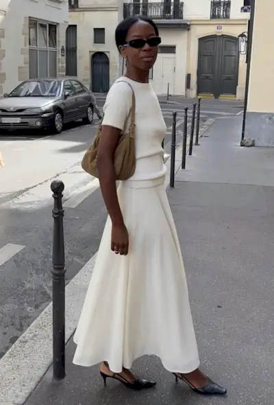 @sylviemus_ wears a white knitted tee, white skirt, black low heels and a brown suede bag