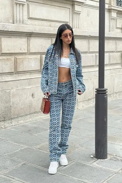 a photo of a club outfit with a woman wearing denim jacket with a white tube top and jeans and tinted Sunglasses and white sneakers
