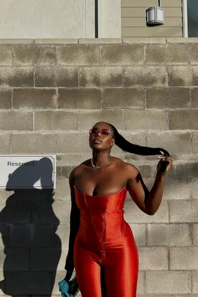 a photo of a club outfit with a woman wearing rimless sunglasses and a red corset top with matching pants and a clutch bag